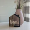 Casita decorativa Home impresa en 3D en negro, arena y crema, junto a un jarrón