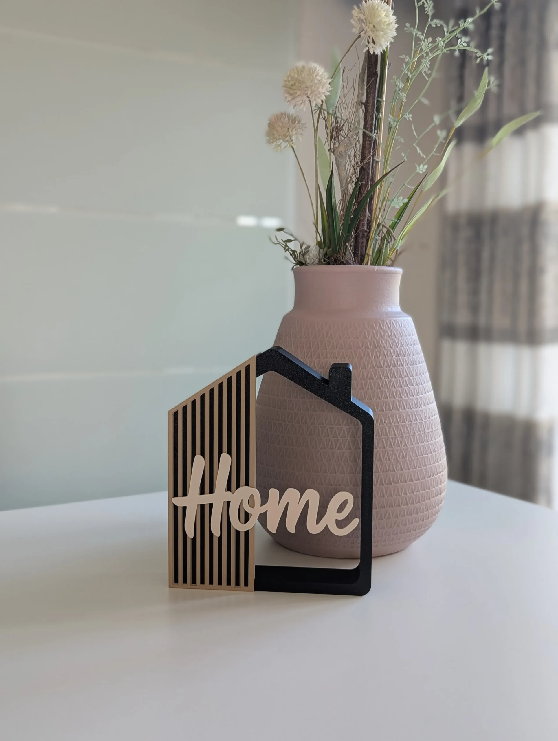 Casita decorativa Home impresa en 3D en negro, arena y crema, junto a un jarrón