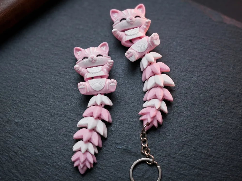 Pareja de llaveros gato articulado rosa y blanco sobre pizarra, uno con anilla